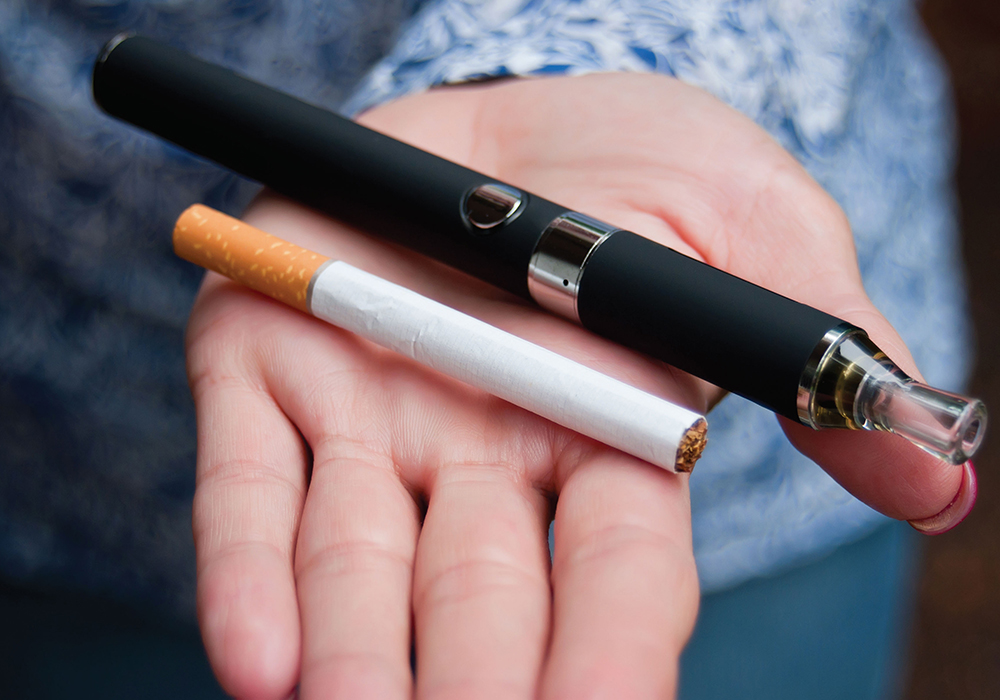 Caucasian White hand holding an e-cigarette vaping device and regular cigarette