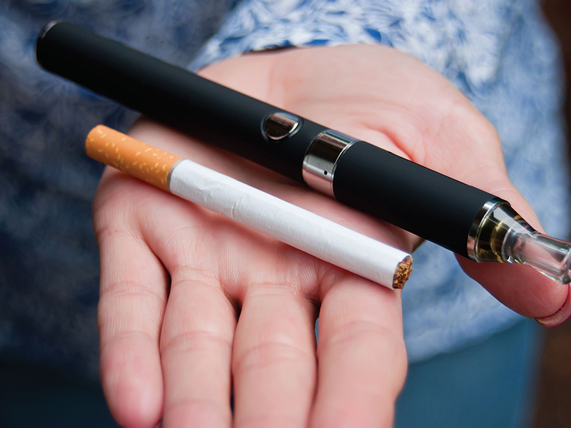 Caucasian White hand holding an e-cigarette vaping device and regular cigarette