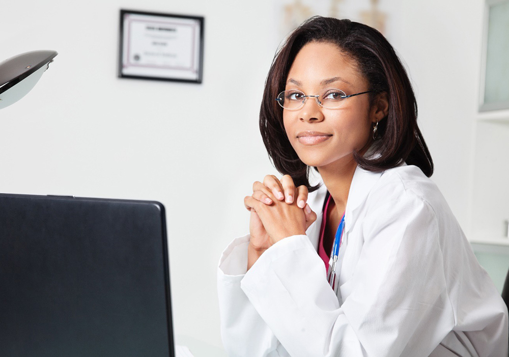 nurse in office with computer screen and certificate on wall