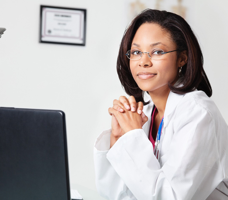 nurse in office with computer screen and certificate on wall