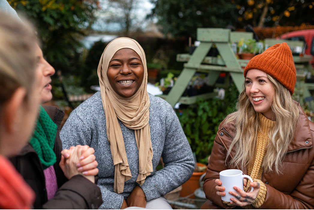 Diverse group of young people sitting outside with mugs in hands